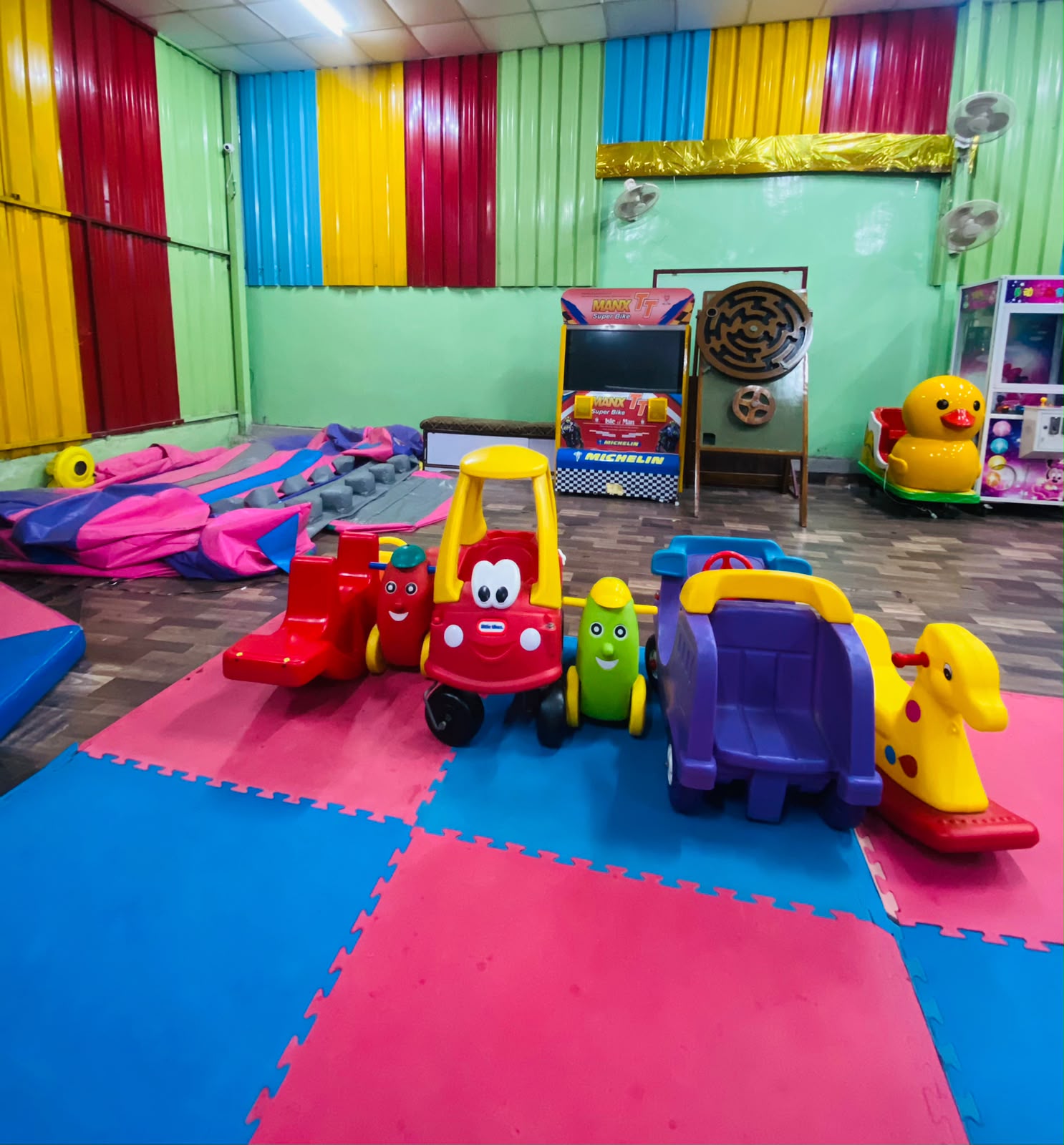 A colorful indoor play area with children's toys, including a bouncy castle and ride-on vehicles.