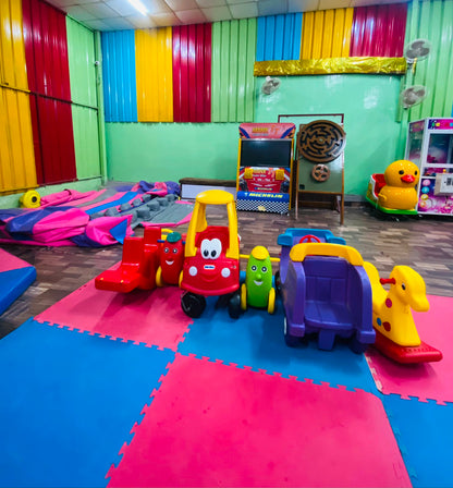 A colorful indoor play area with children's toys, including a bouncy castle and ride-on vehicles.