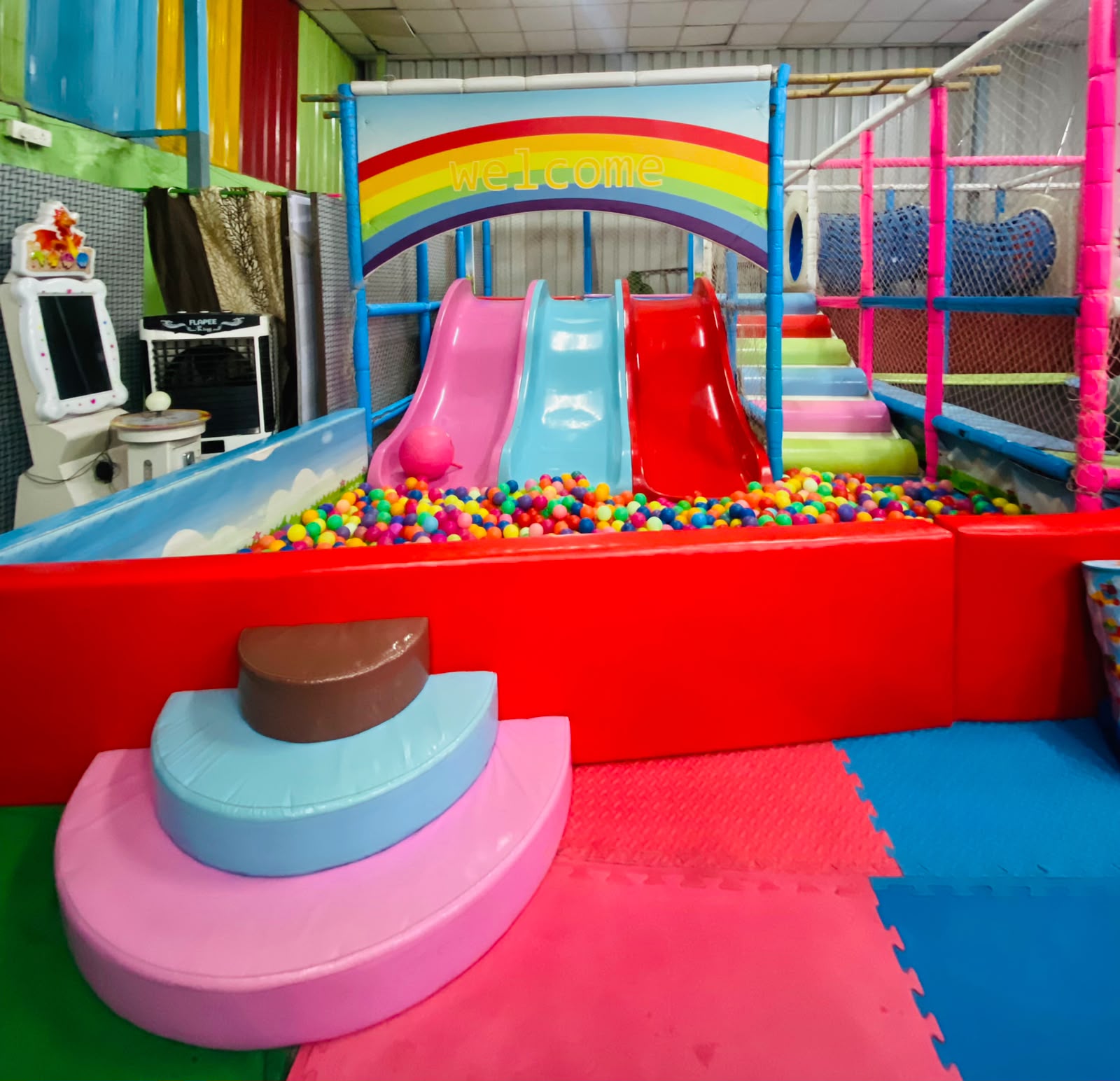 A colorful indoor playground with slides, a ball pit, and soft play structures for children.
