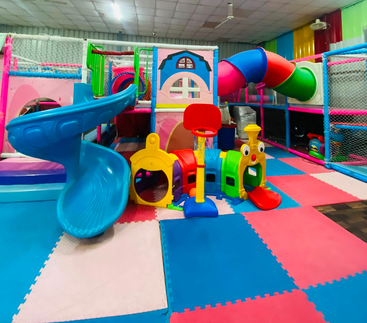 A colorful indoor playground with slides, tunnels, and a basketball hoop for young children.