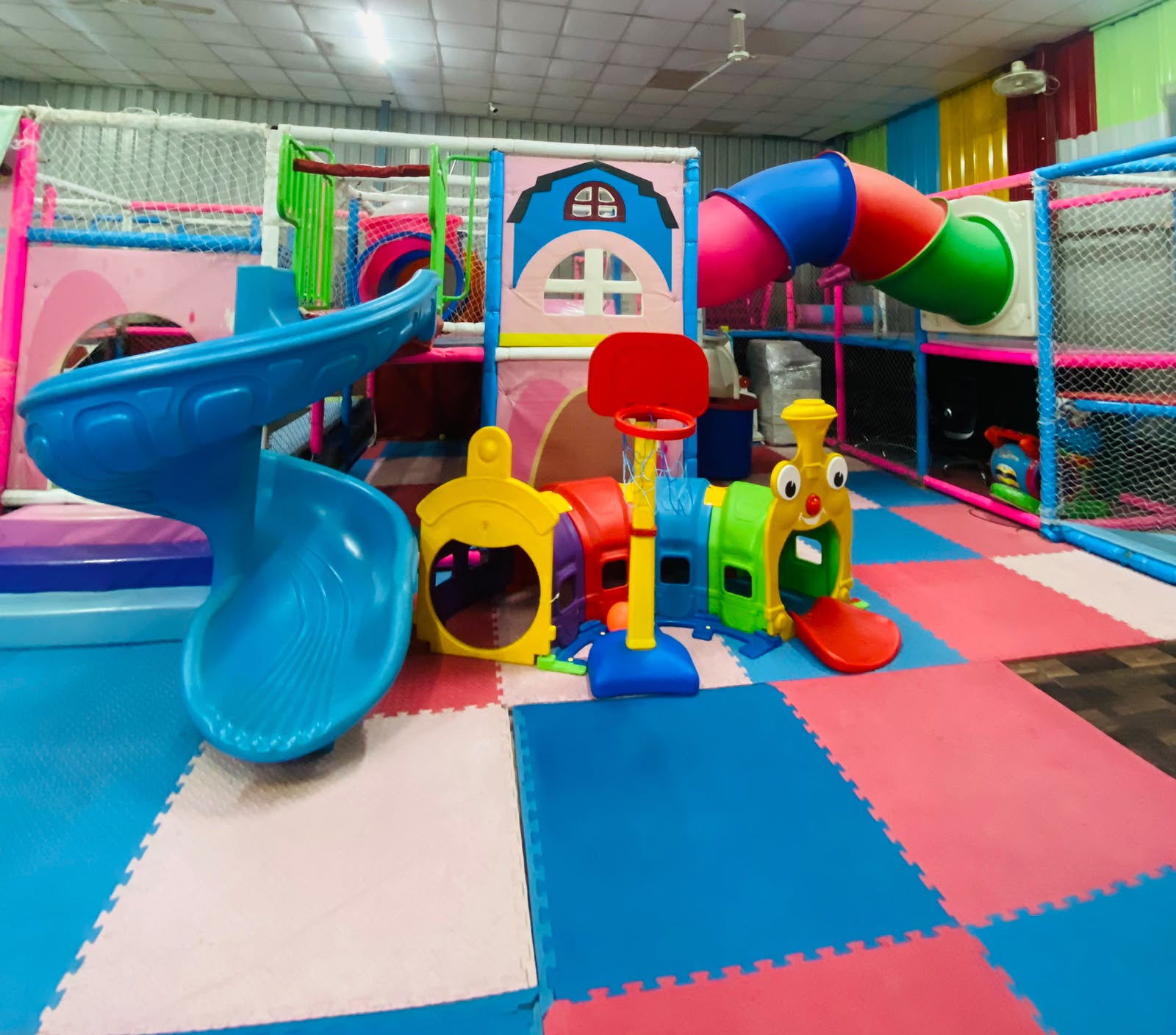 A colorful indoor playground with slides, tunnels, and a basketball hoop for young children.