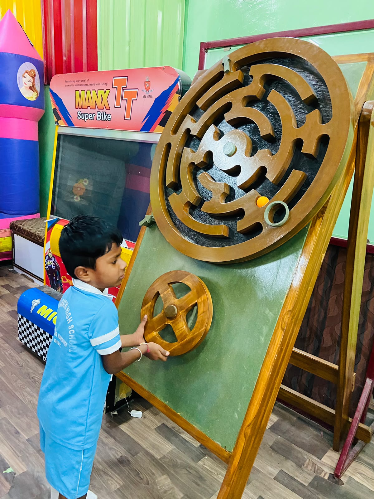 A young boy plays a wooden maze game with a ball, his hands on a steering wheel.
