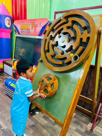 A young boy plays a wooden maze game with a ball, his hands on a steering wheel.