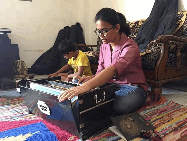 Woman playing a harmonium with a child in a room with colorful rugs and furniture.