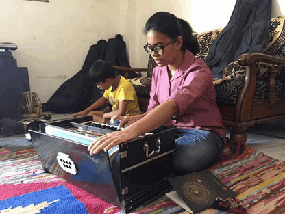 Woman playing a harmonium with a child in a room with colorful rugs and furniture.