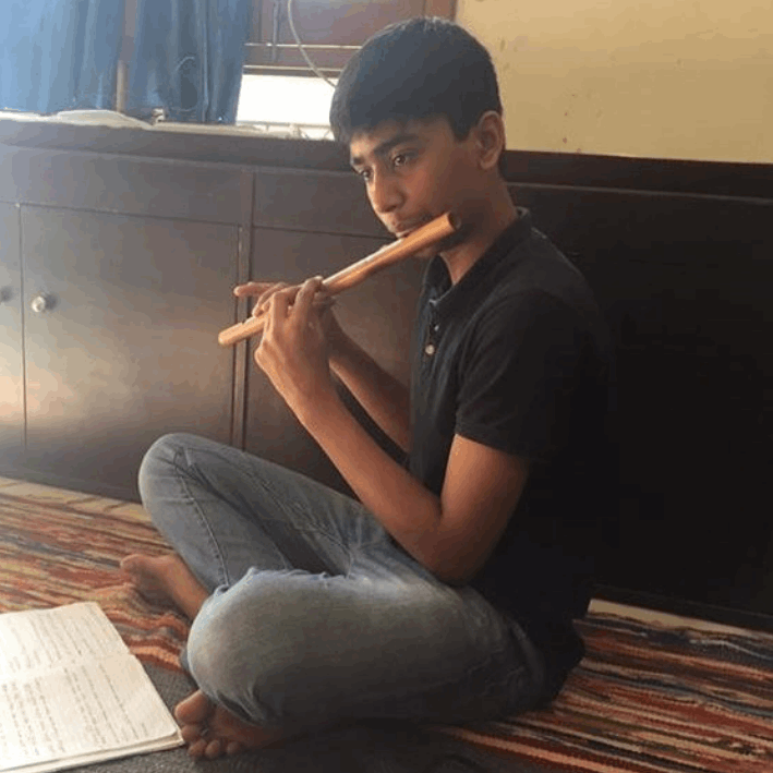 Person playing a flute on a colorful rug with a cabinet and window in the background