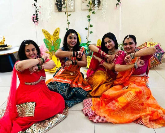 Four women in traditional Indian sarees posing for a dance form together in a decorated indoor setting.