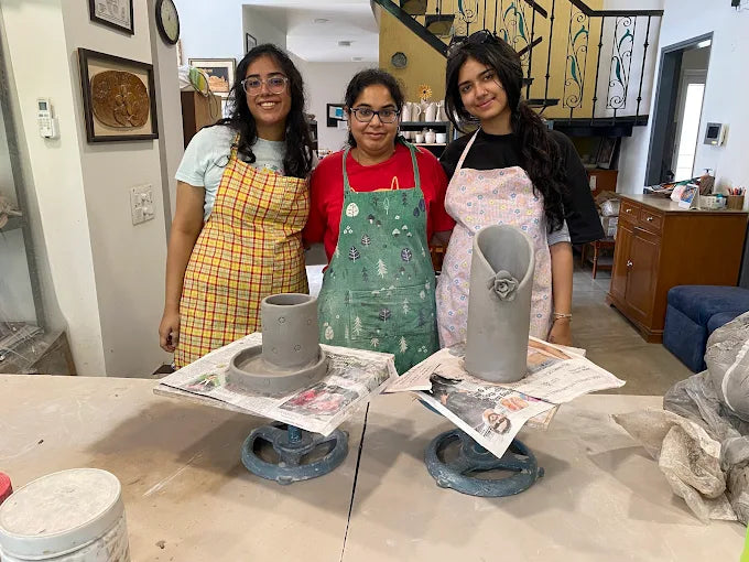 Three individuals in a pottery studio with clay pots and tools on a table.