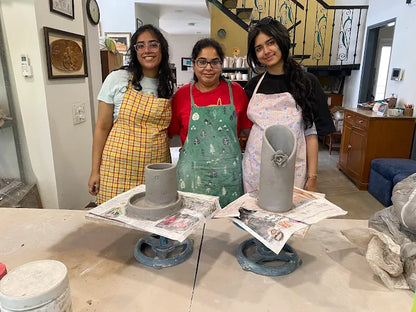 Three individuals in a pottery studio with clay pots and tools on a table.