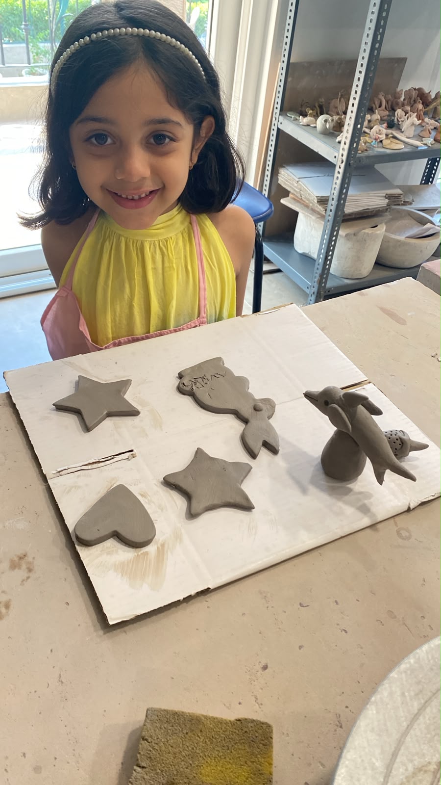 A young girl smiles while working on clay sculptures of sea creatures and stars.