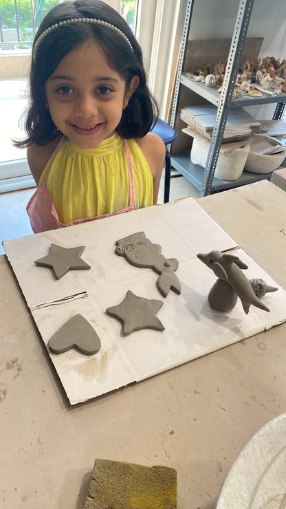 A young girl smiles while working on clay sculptures of sea creatures and stars.