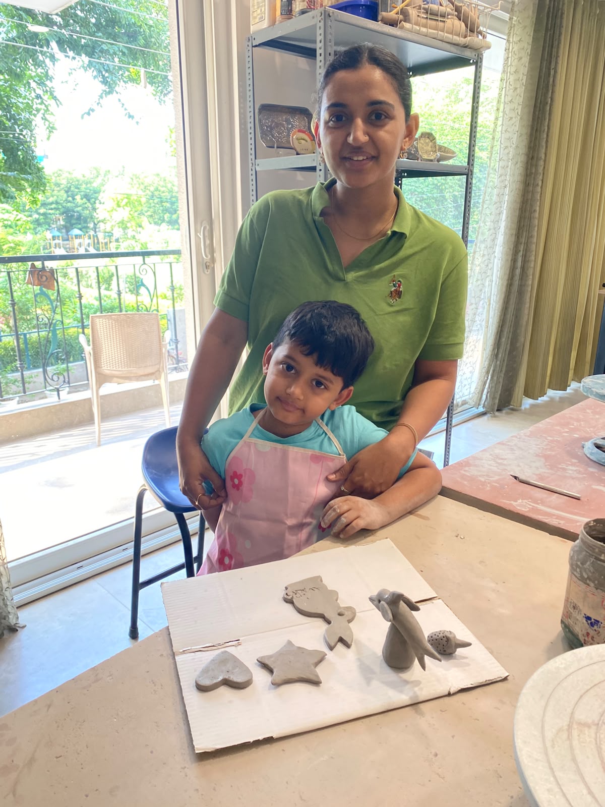 A woman and a young boy pose with clay creations on a table in a studio.