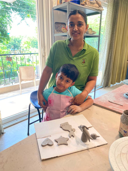 A woman and a young boy pose with clay creations on a table in a studio.