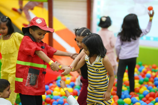 Children in a ball pit play together, with one dressed as a firefighter.