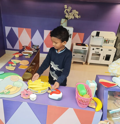 A young boy plays with toy food in a pretend kitchen and grocery store.