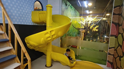 A young child slides down a yellow playground slide in a room with a deer display.