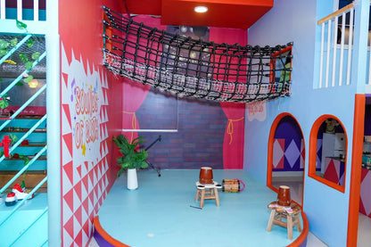 A colorful indoor play area with a rope bridge, drums, and a plant.