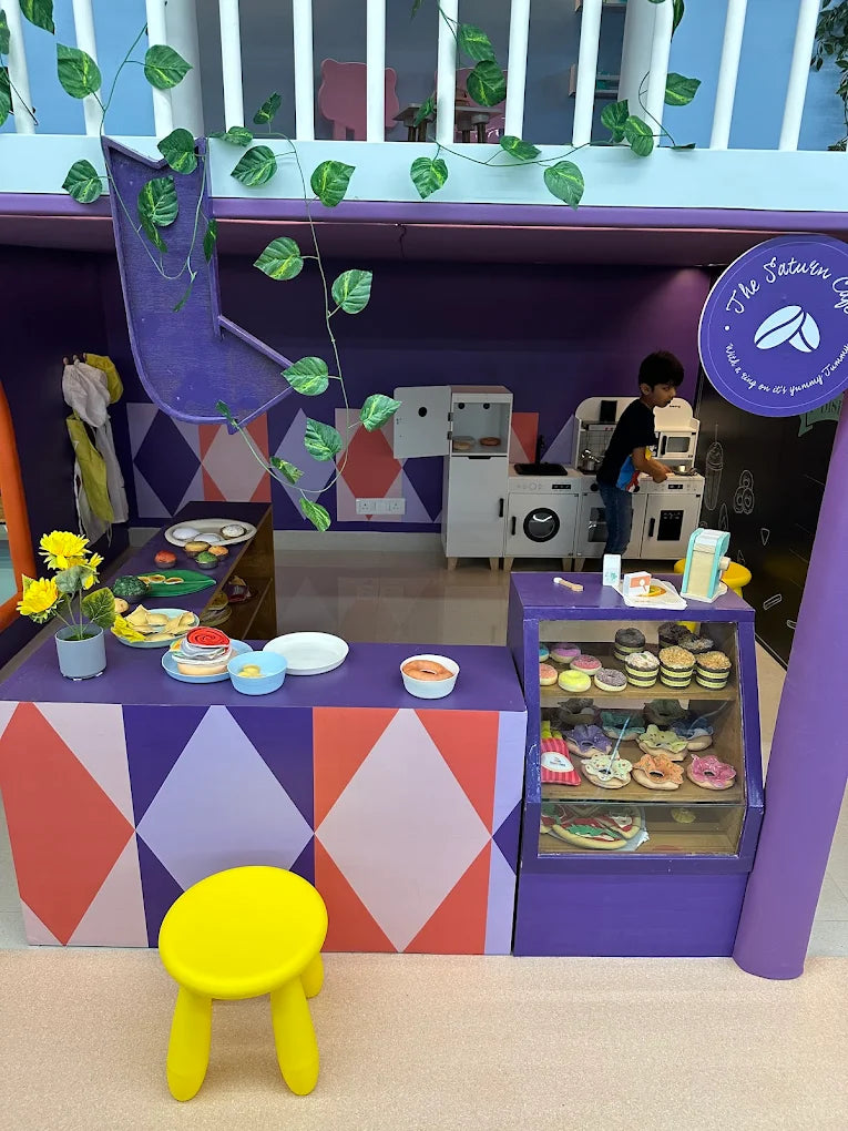 A young boy plays in a colorful pretend cafe with toy food.