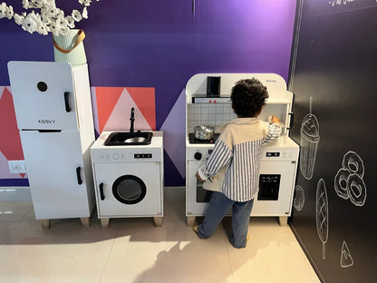 A young child plays with a toy kitchen set in a room with purple walls and chalk drawings.