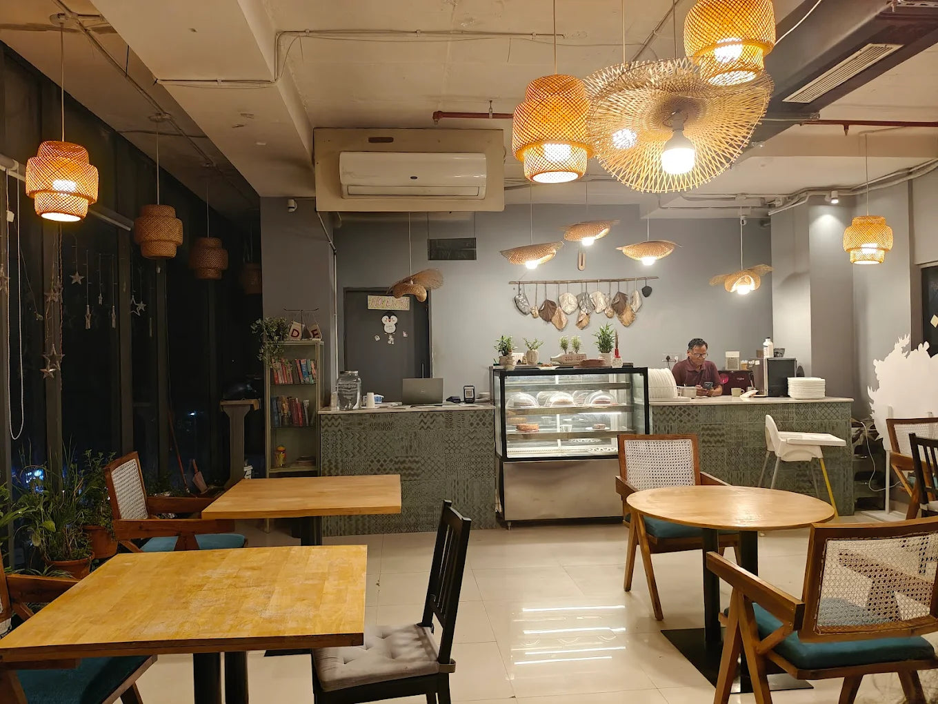 A man sits at a counter in a cafe with bamboo light fixtures and wooden tables.