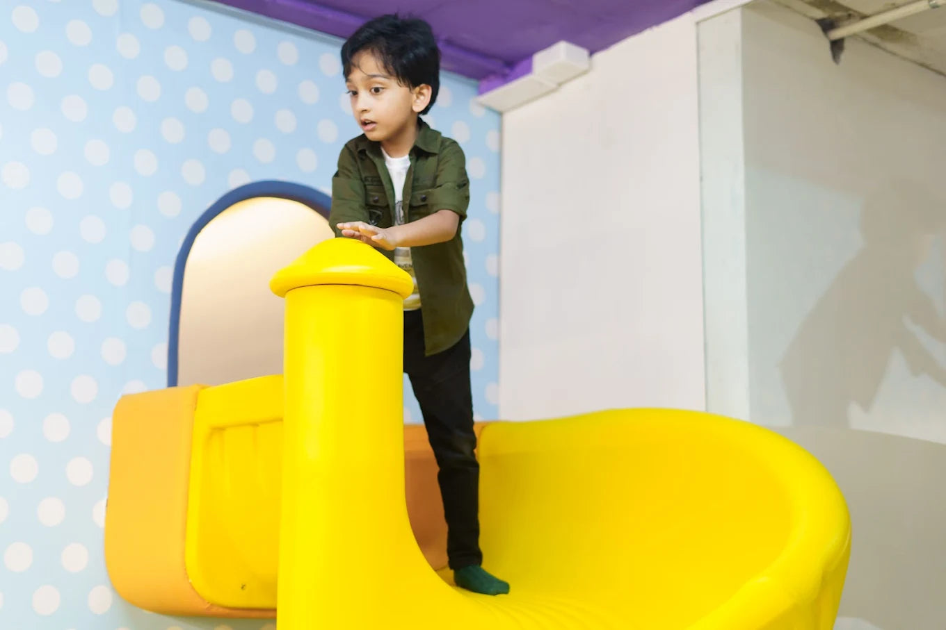 A young boy stands on a bright yellow slide in a playful indoor setting.