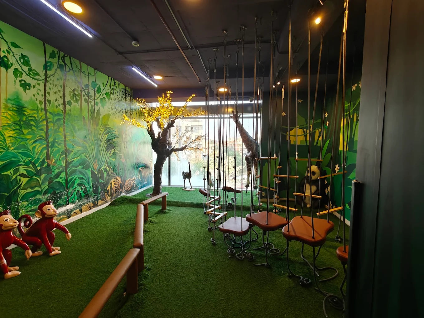 A jungle-themed indoor play area for children with monkey figures, swings, and animal decorations.