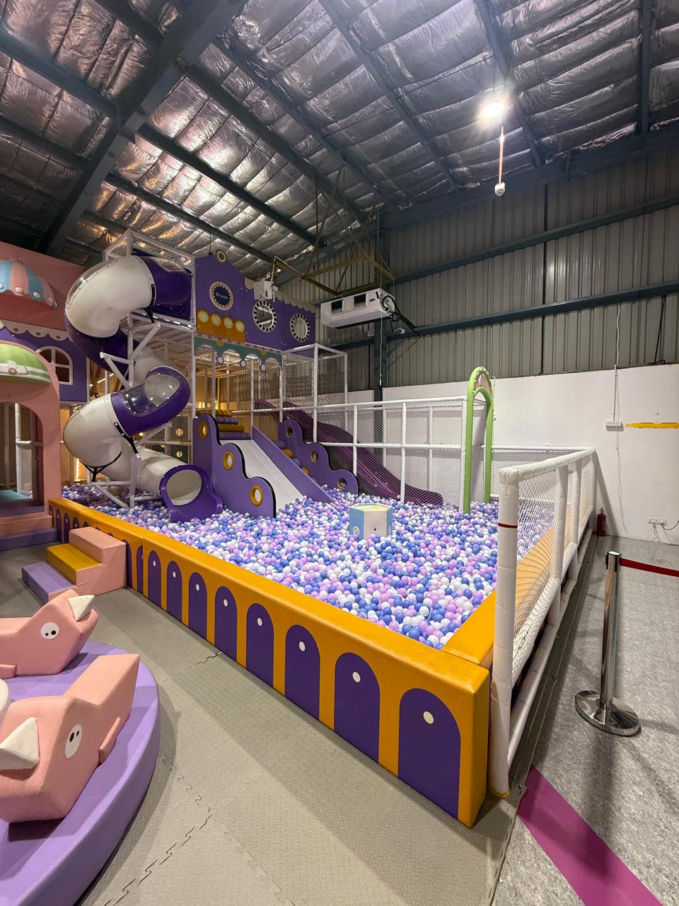 A colorful indoor playground with slides, a ball pit, and soft play structures for young children.