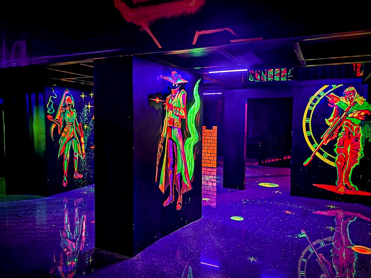 Neon characters on black walls in a dark laser tag arena.