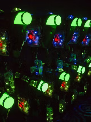 Laser tag phasers with glowing green lights in a dark arena.