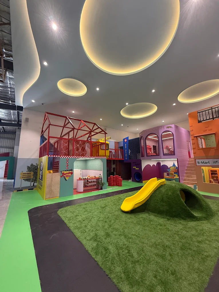 A colorful indoor playground with a slide, climbing structure, and play shops for children.
