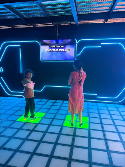 Two children stand on a glowing floor in front of a screen that says "FIND THE COLOR."