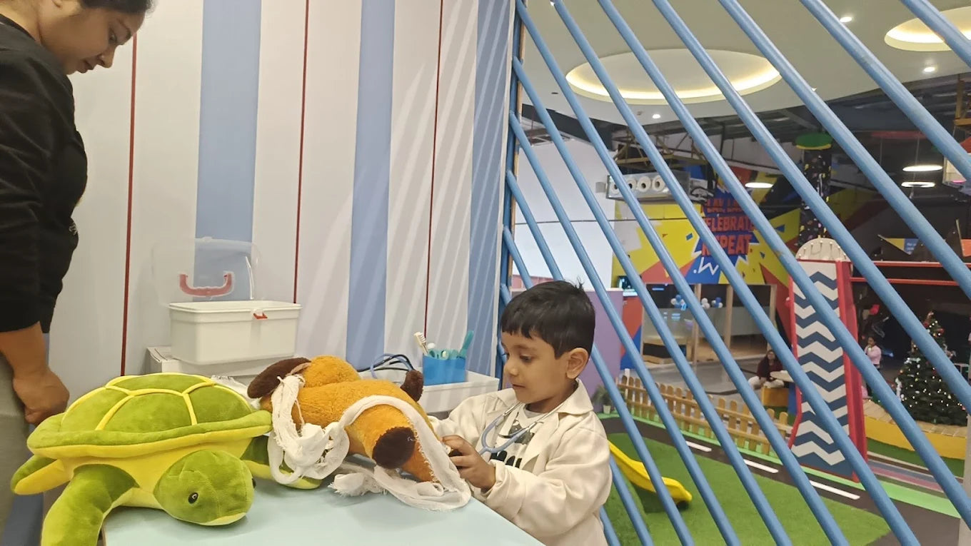 A young boy dressed as a doctor plays with stuffed animals in a colorful indoor play area.