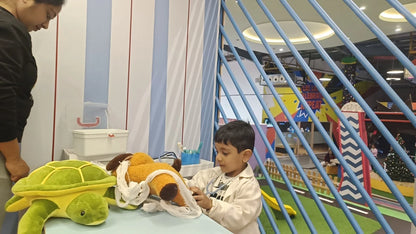 A young boy dressed as a doctor plays with stuffed animals in a colorful indoor play area.