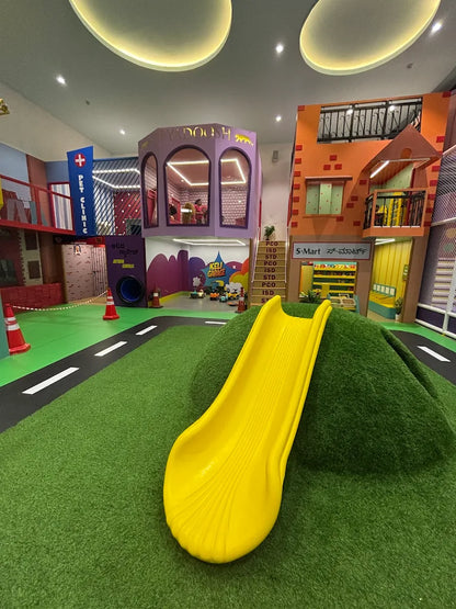 A colorful indoor playground with a yellow slide, miniature buildings, and children playing.
