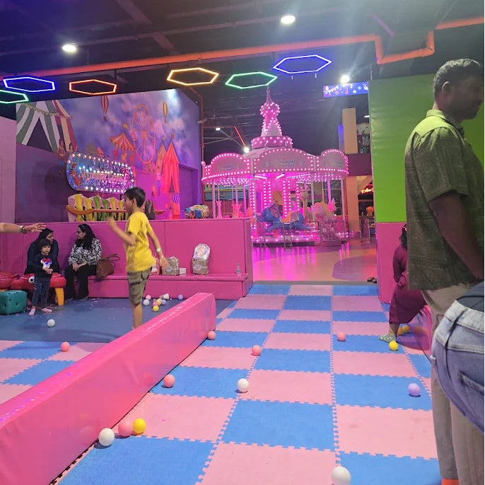Children play in a brightly lit indoor amusement area with a carousel and colorful hexagonal lights.