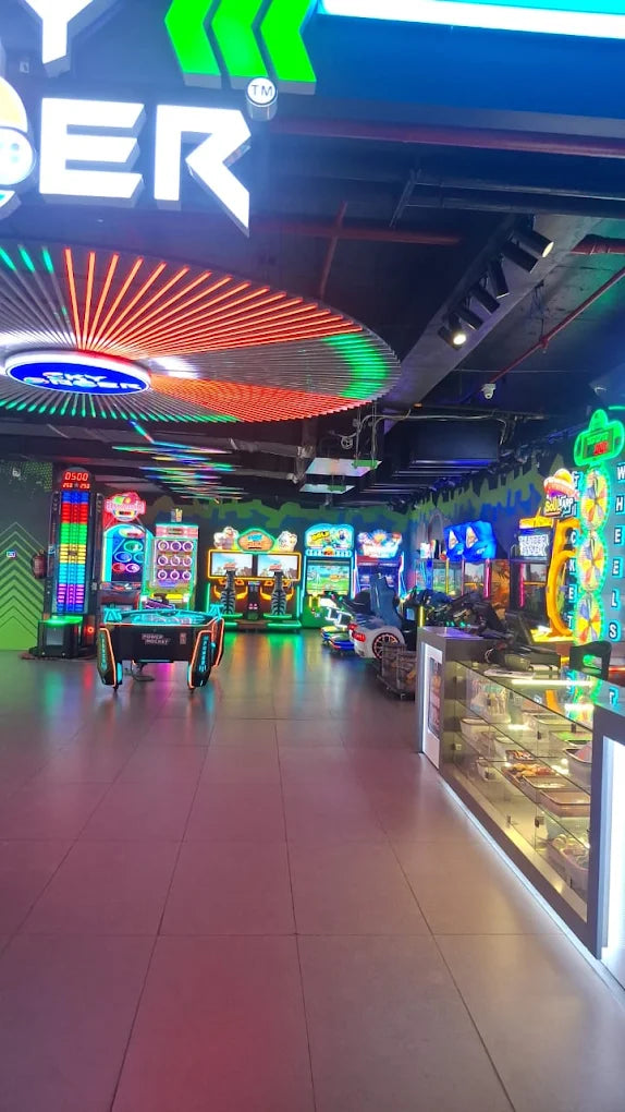 Vibrant arcade game zone with neon lights, racing simulators, and ticket redemption counter at Sky Gamer Sector 12 Faridabad