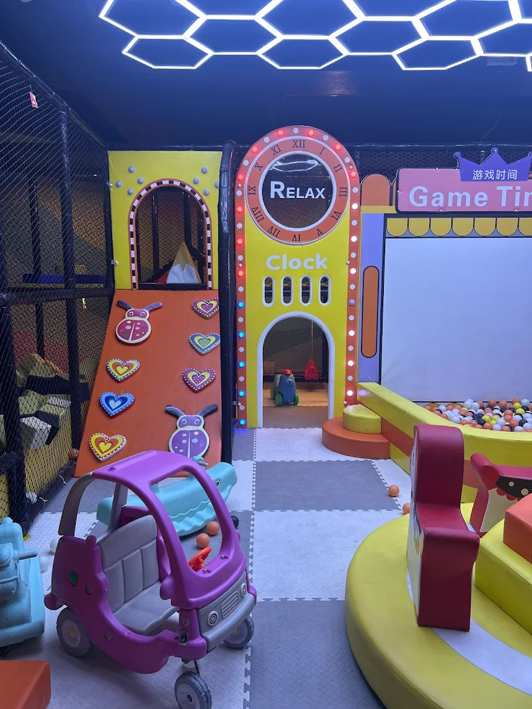 Indoor play area with toy car, colorful climbing wall, and ball pit under neon hexagonal ceiling lights at Sector 12 Faridabad