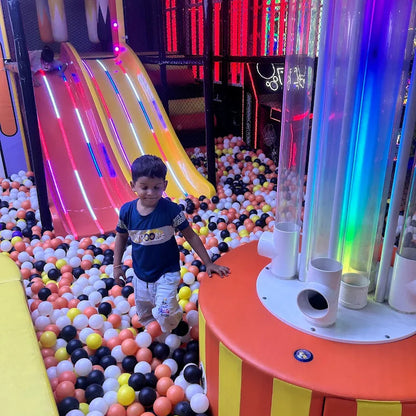 Child playing in a colorful ball pit with slides and lights in the background