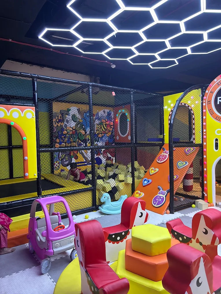 Indoor kids play area with cushioned climbing structures, slides, and neon hexagon lights at Sector 12 Faridabad arcade zone