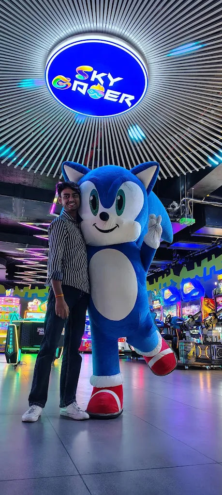 Man posing next to a Sonic the Hedgehog mascot under illuminated Sky Gamer logo at arcade game zone Sector 12 Faridabad