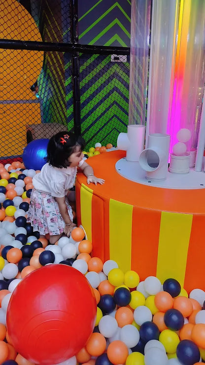 Child playing with colorful balls in a ball pit with a vibrant background