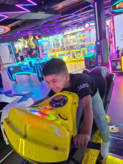 Young boy riding bright yellow motorcycle arcade game amid vibrant neon-lit Sky Gamer Zone Faridabad