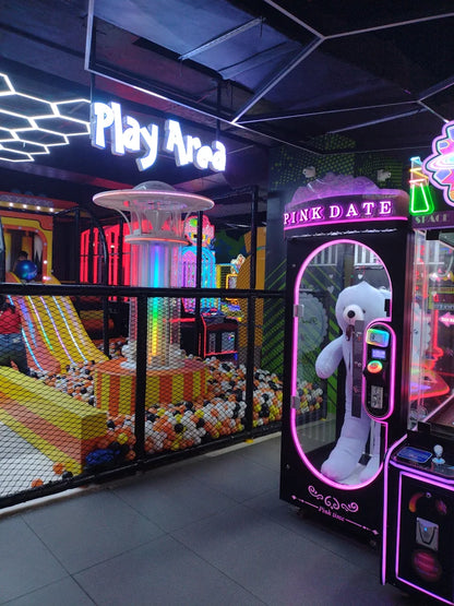 Neon-lit arcade claw machine with white bear prize next to ball pit and colorful slide at Sector 12 Faridabad play zone
