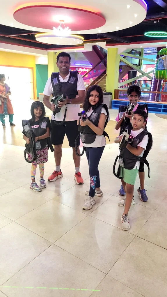 A family plays laser tag in an indoor amusement center, wearing vests and holding phasers.