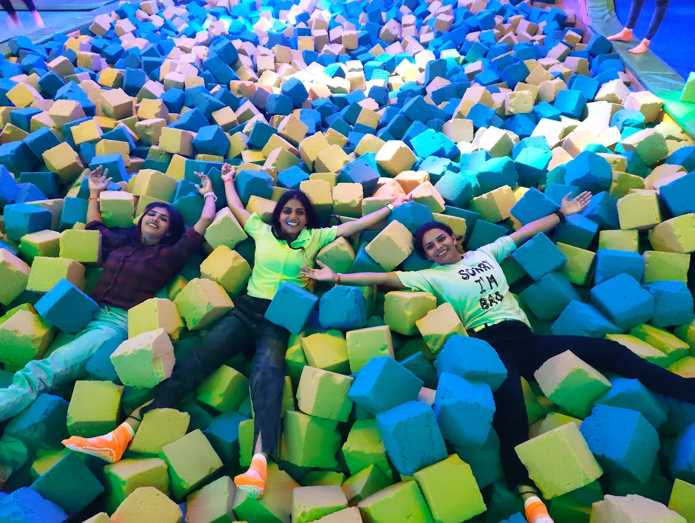 Three young women lie in a foam pit, smiling and posing for a photo.