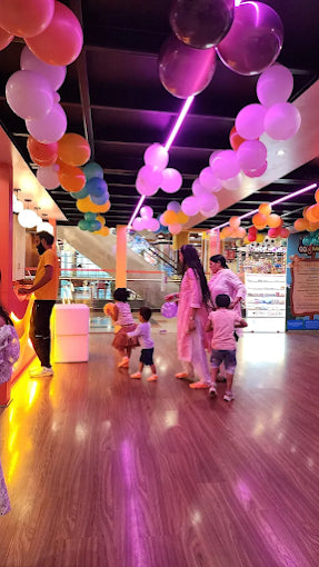 Families and children walking under colorful balloon arches in a lively indoor play area at a trampoline park