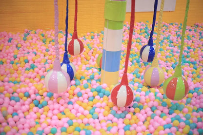 Colorful hanging soft balls over a large multicolored ball pit in a vibrant indoor kids play area
