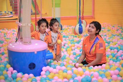 Woman and two children playing with colorful balls around soft play equipment in an indoor kids play zone