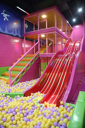 Indoor children’s play area featuring bright red slides leading into a pastel-colored ball pit at a trampoline park
