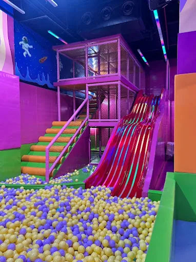 Bright indoor playground with triple red slides and a pastel ball pit in a kids entertainment zone